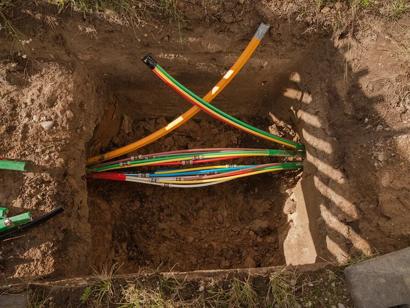 Bundled colored conduits entering the ground at an excavated bore pit